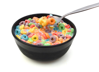 Delicious and nutritious fruit cereal loops flavorful in black bowl and milk and spoon on white background, healthy and funny addition to kids breakfast