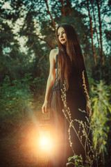Fototapeta premium Beautiful witch with the magic lantern invites you into the forest.