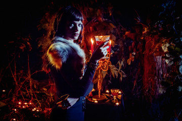 Beautiful witch with the glass of vine on the night forest background.