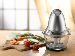 mini food processor and chopped vegetables on a wooden table. light comes from a window in the...