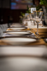 Dinner plates and wine glasses on a long table with a shallow depth