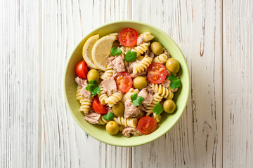 Fusilli pasta salad with tuna, tomatoes, olives and parsley on white wooden background.