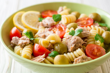 Fusilli pasta salad with tuna, tomatoes, olives and parsley on white wooden background.