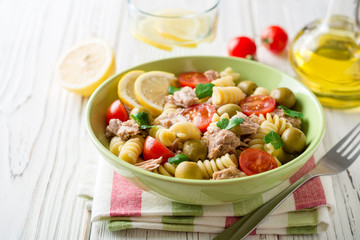 Fusilli pasta salad with tuna, tomatoes, olives and parsley on white wooden background.