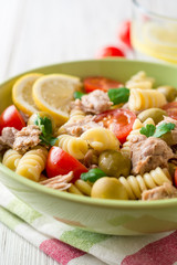 Fusilli pasta salad with tuna, tomatoes, olives and parsley on white wooden background.