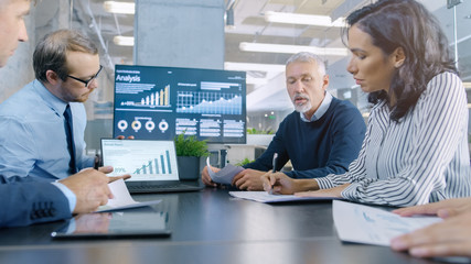 Obraz premium Diverse Group of Successful Business People in the Conference Room, Work on a Company's Growth, Share Charts and Statistics. In the Background Wall TV with Corporate Data on it.