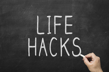 Human hand writing life hacks words on the blackboard with white chalk on blackboard