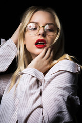 Elegant blonde woman in glasses wearing blouse with naked shoulders, posing with dramatic studio light