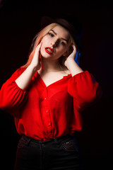 Luxurious young woman wearing red blouse and hat posing in the shadow with blue and red light