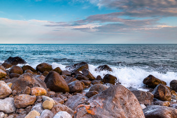 Sea surf at sunset - waves break against stones