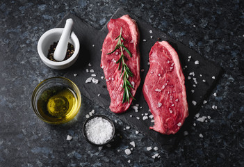 Two raw picanha steaks on a cutting board with spices on a dark background