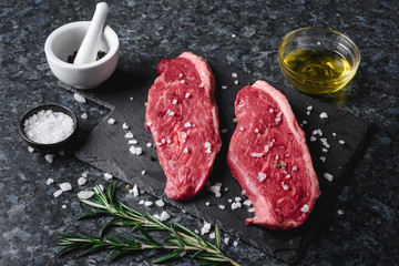 Two raw picanha steaks on a cutting board with spices on a dark background