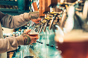 Hand of bartender pouring a large lager beer in tap.