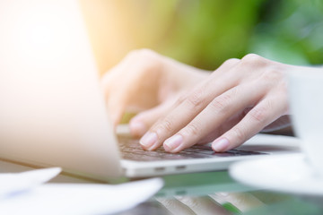 Asian woman hands has touching and typing on laptop computer with blurred coffee, computer and view outside window.