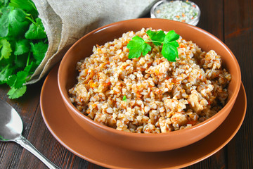 Boiled buckwheat in a bowl with pieces of chicken meat and cilantro on a brown wooden table.