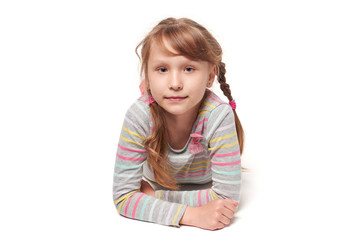 Front view of a child girl lying on stomach on the floor looking at camera, over white background