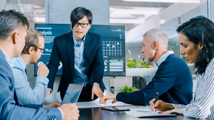 In the Conference Room Asian Branch Businessman Representative Spreads Market Expansion Project Blueprint on the Table Before Board of the Directors.