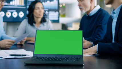 In the Meeting Room Laptop with Green Chroma Key Screen on the Conference Table. In the Background Business People Have Important Discussion.