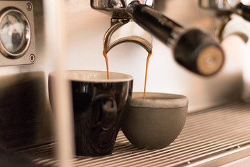 Espresso dripping out of the machine into an espresso and cappuccino cup
