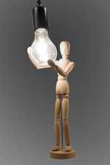  wooden person holds the burning electric bulb in hand