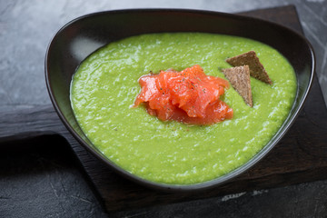 Black bowl of green peas cream-soup with addition of salmon, selective focus, studio shot, close-up