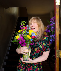 Woman with long blond hair and colorful dress received delivered flowers at front door with spring wreath on door
