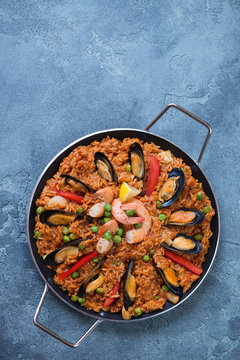 Frying pan with seafood paella on a blue stone background, vertical shot with space, above view