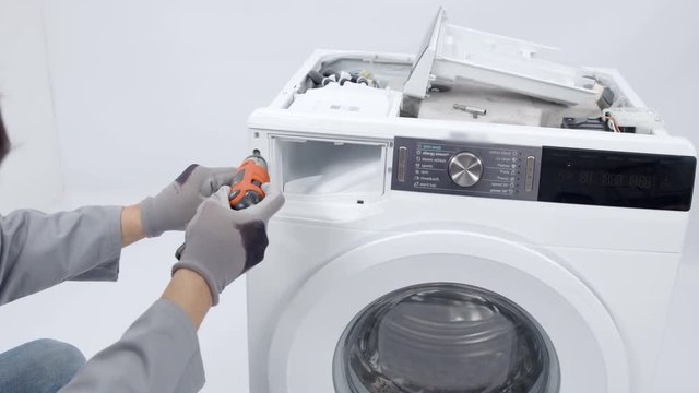 A repairman is dismantling a washing machine and he is taking out screws. He needs to fix the device.