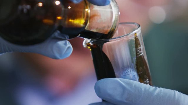 Assistant Pours Raw Oil from Bulb into Lab Glass