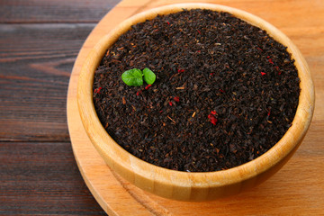 Black dry tea with a cherry in a bowl on a wooden table.