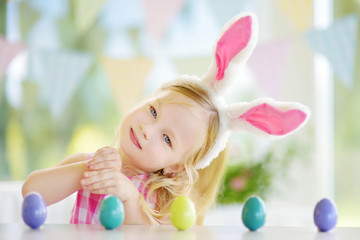 Fototapeta na wymiar Cute little girl wearing bunny ears playing egg hunt on Easter