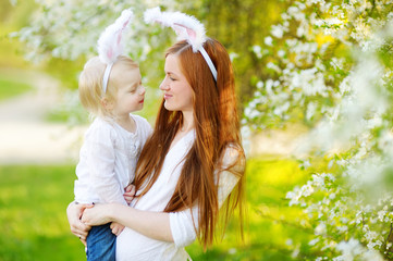 Young mother and her daughter wearing bunny ears in a spring garden on Easter day