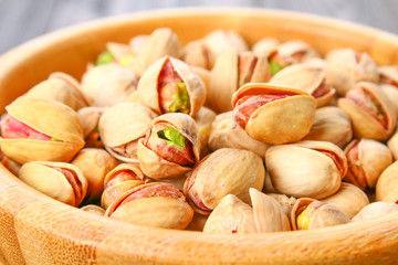 Dish full of pistachios with more pistachios on side.