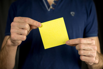 Man holds blank yellow sticker. Thumb up, blue T-shirt. close-up, selective focus