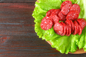 Smoked sausage, salami chopped in slices on a salad on a wooden circular cutting board on a brown table.