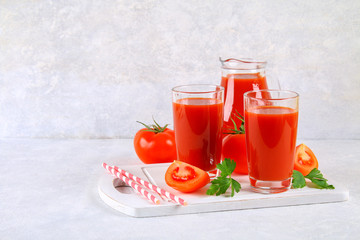 Tomato juice in glasses and a pitcher on a gray concrete table.