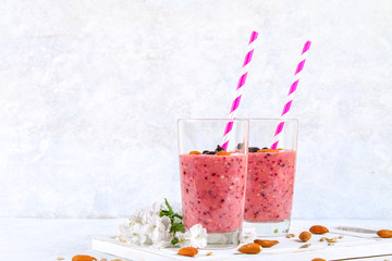 Blueberry smoothies of berries, banana and almonds in glasses with cocktail tubes on a white wooden board.