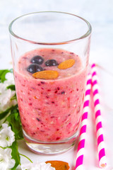 Blueberry smoothies of berries, banana and almonds in glasses with cocktail tubes on a white wooden board.