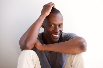 smiling young african american man sitting by white wall and thinking