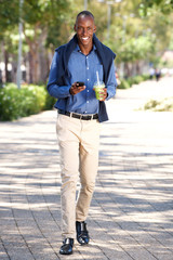 Full length happy african american man walking with mobile phone outdoors