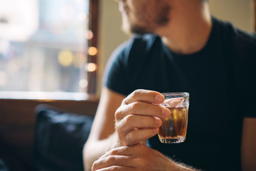 A glass with a cold refreshing brown tea in the hand of a man in the background of a cafe.