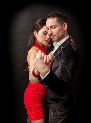Attractive couple of professional dancers dancing passionate tango on dark background