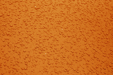 Water drops on blue color metal surface with blur effect in orange color.