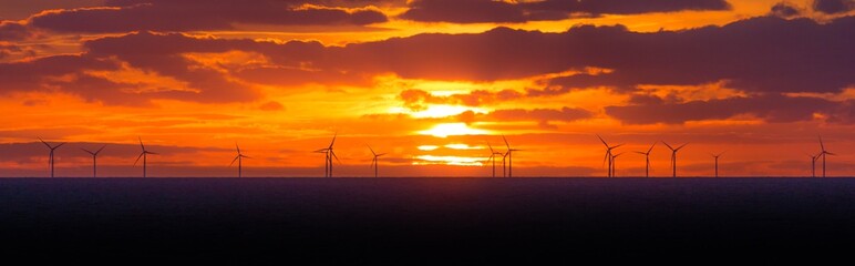 Fototapeta na wymiar Panorama Sonnenuntergang mit Windräder in Offshore Windpark. Viele Windkraftwerke im Meer und Wolken im Himmel. Strom, der nachhaltig, alternativ, erneuerbar, grün ist und Klimawandel verhindert