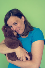 Pregnant woman posing with a plush toy imitating baby in front of green background.