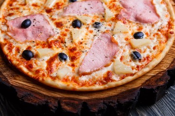Hot pizza with ham and black olives served on chopped wood, close up. Italian food, restaurant menu concept
