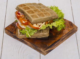 Waffles sandwich with chicken, vegetables and cheese on wooden background