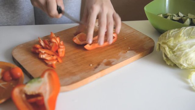a woman is cutting a paprika with a knife on a wooden board.