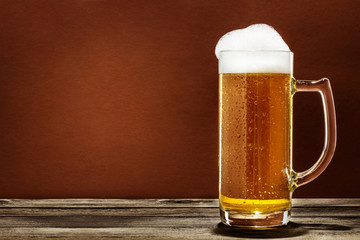 A Glass Of Foaming Beer On A Wooden Table Isolated On Brown Background