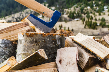 Axe standing against a piled pieces of firewood with beautiful nature in the background.